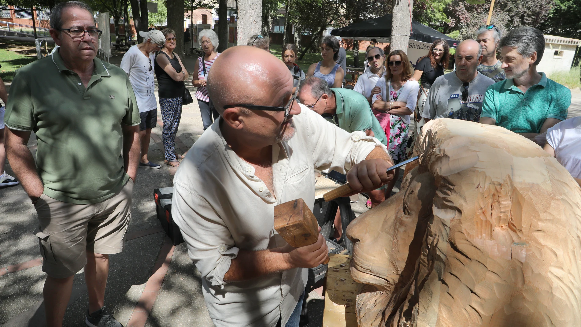 El escultor Alfredo Martín 'Chis' talla la cabeza de un león rodeado de visitantes de la exposción