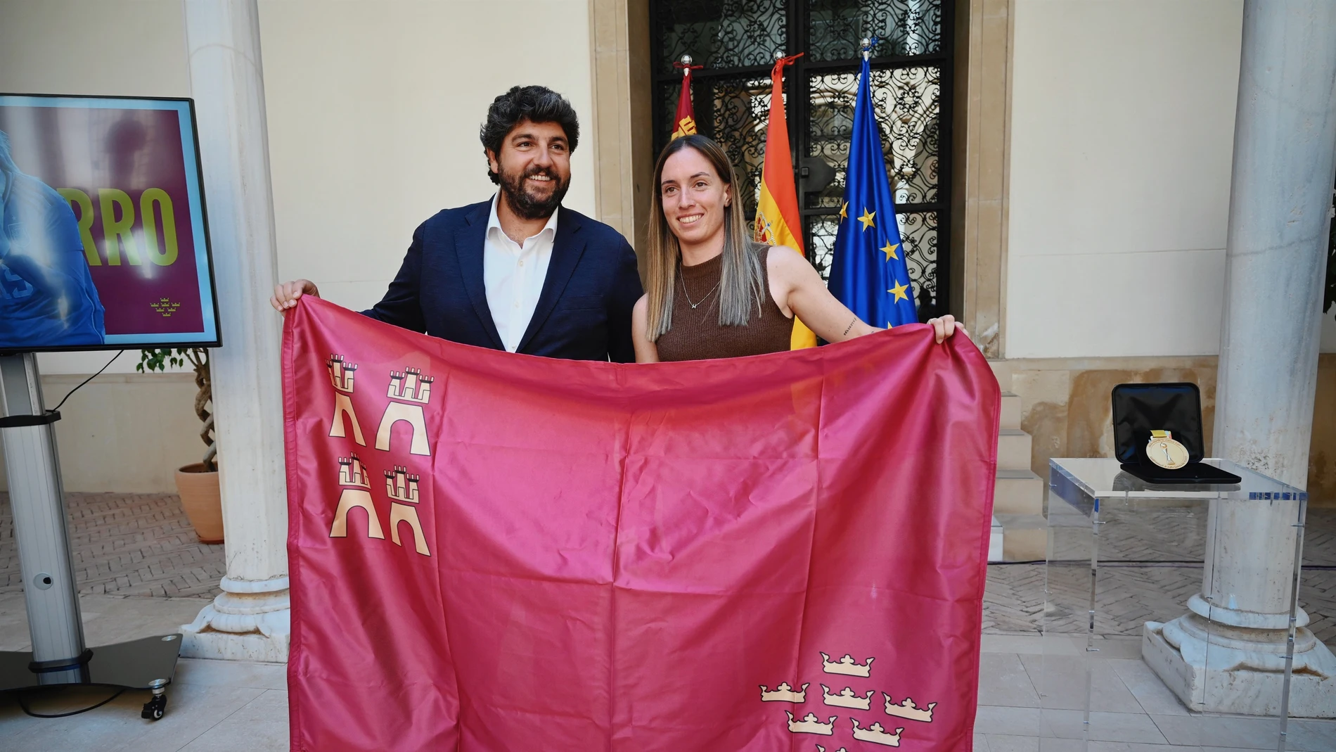 El jefe del Ejecutivo autonómico en funciones, Fernando López Miras, y la campeona del Mundial de Fútbol Femenino, la yeclana Eva Navarro, posan con una bandera de la Región de Murcia