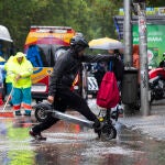 Fuertes lluvias en Madrid por el paso de la Dana. Un joven cruza con su patinete eléctrico por un paso de peat