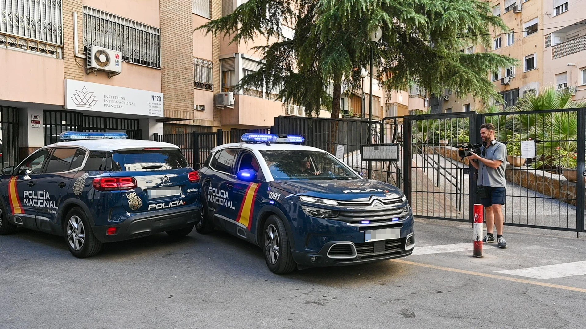 Un reportero graba imágenes de los patrulleros de la Policía Nacional en la entrada de la vivienda de la mujer localizada este domingo en Granada muerta con signos de violencia después del suicidio de un hombre, quién se arrojó desde un balcón en esa misma calle, falleciendo en el acto.