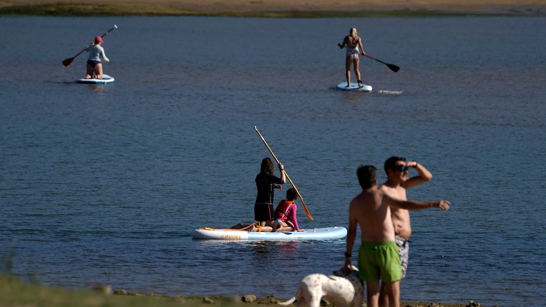 Varias personas sobre unas tablas de paddle suf en la playa de Misiego al atardecer