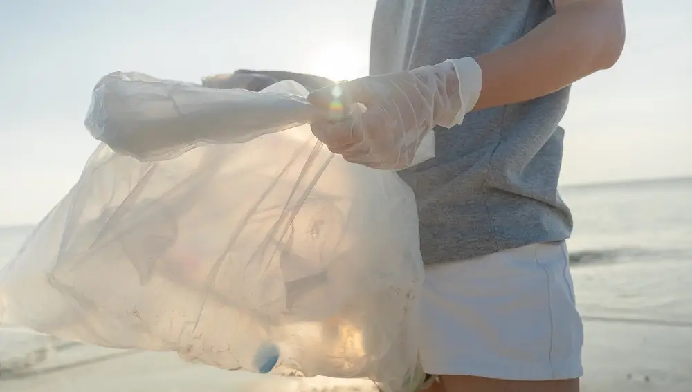 Voluntario recogiendo envases de plástico en la playa. 