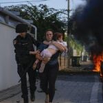 Police officers evacuate a woman and a child from a site hit by a rocket fired from the Gaza Strip, in Ashkelon, southern Israel, Saturday, Oct. 7, 2023. The rockets were fired as Hamas announced a new operation against Israel. 