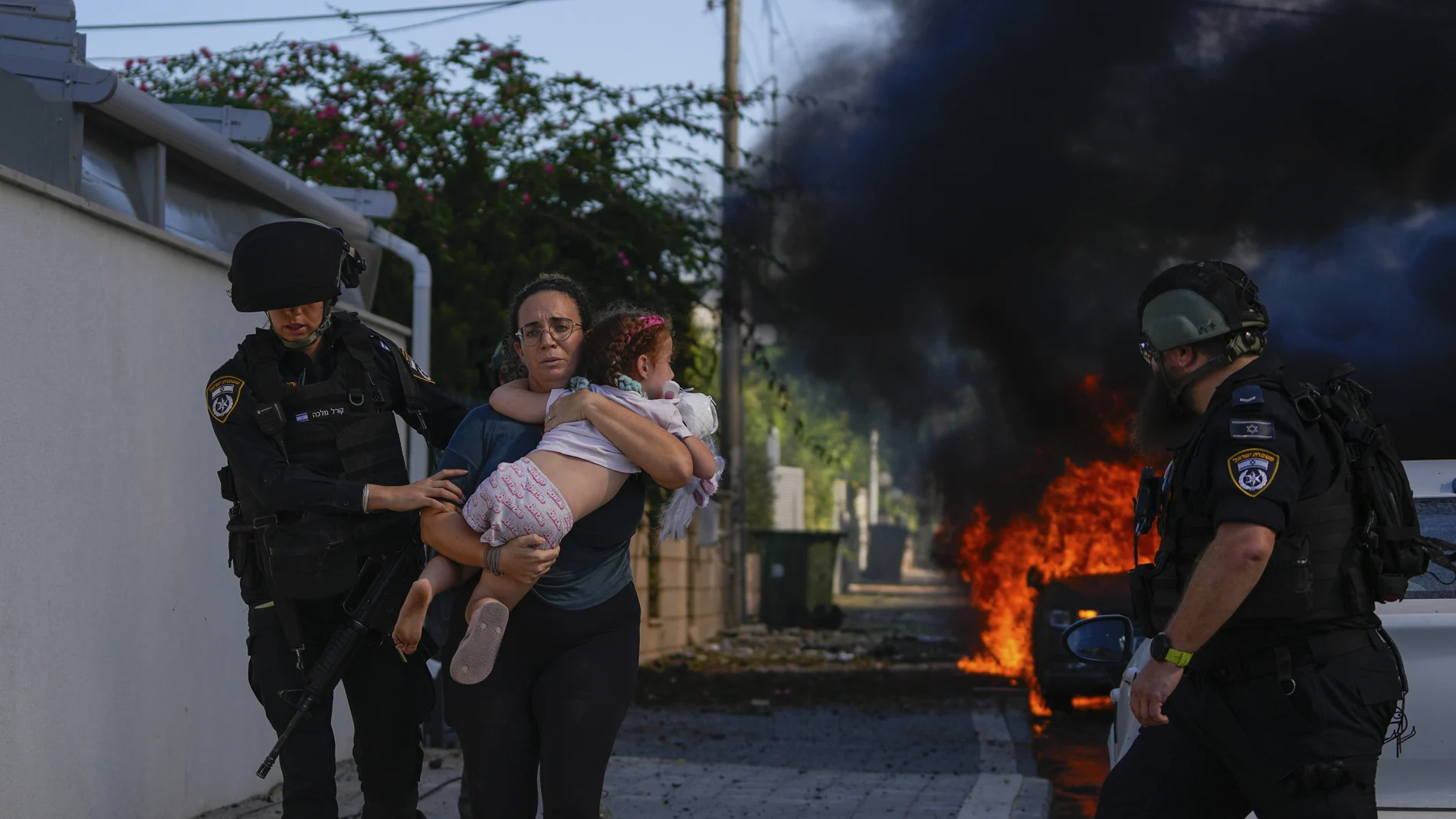 Police officers evacuate a woman and a child from a site hit by a rocket fired from the Gaza Strip, in Ashkelon, southern Israel, Saturday, Oct. 7, 2023. The rockets were fired as Hamas announced a new operation against Israel. 