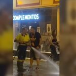 Un trabajador de la limpieza da un manguerazo a una mujer para que se aparte
