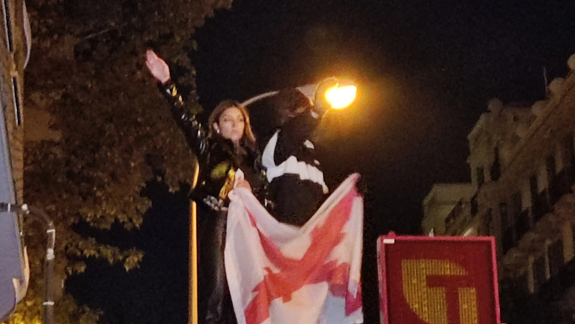 Isabel Peralta realizando el saludo romano y sosteniendo una bandera con la Cruz de Borgoña