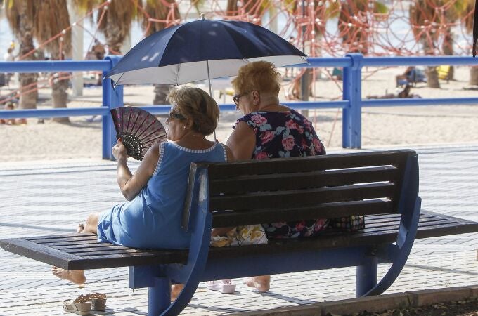 Imagen de dos mujeres protegiéndose del sol y del calor con abanico y parasol.