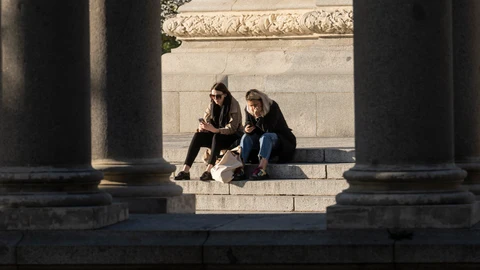 Dos jóvenes miran su móvil en El Retiro