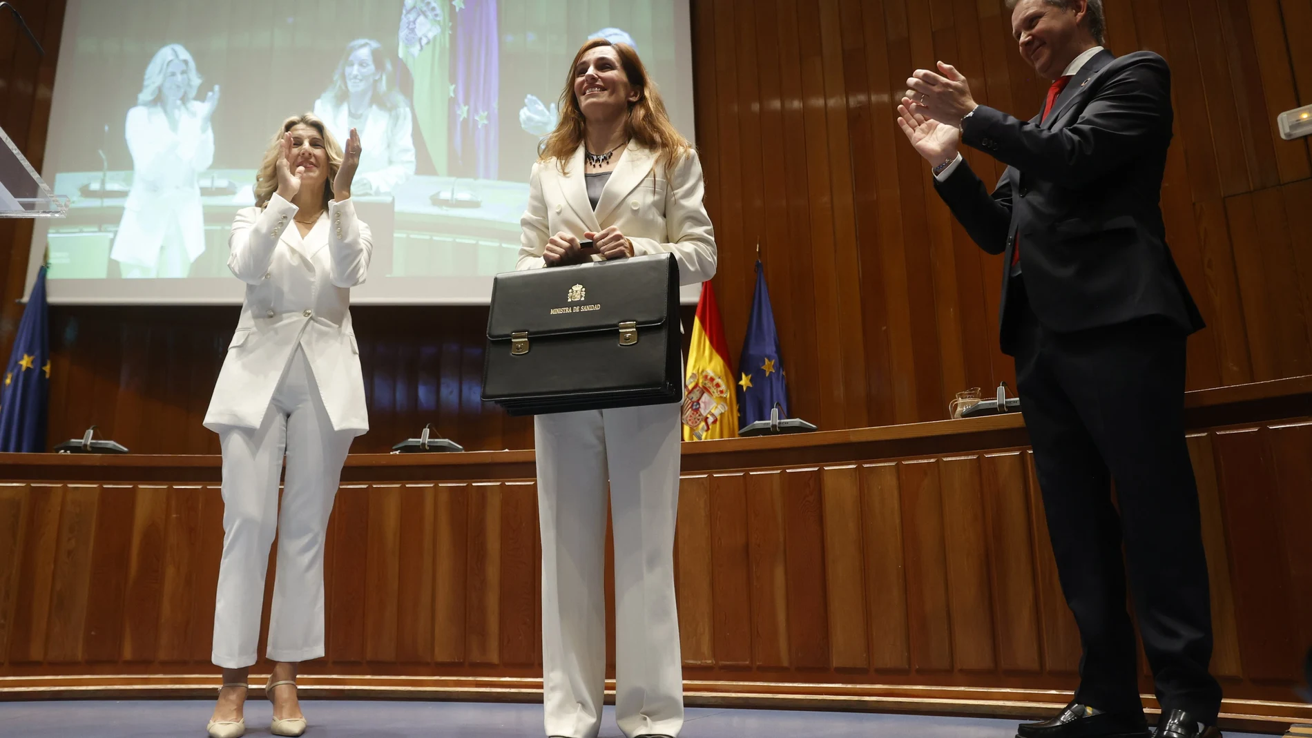 La nueva ministra de Sanidad, Mónica García (c), acompañada de la vicepresidenta segunda Yolanda Díaz (i), recibe su nueva cartera a manos del ex ministro José Miñones, durante la toma de posesión de su cargo, este martes en Madrid.