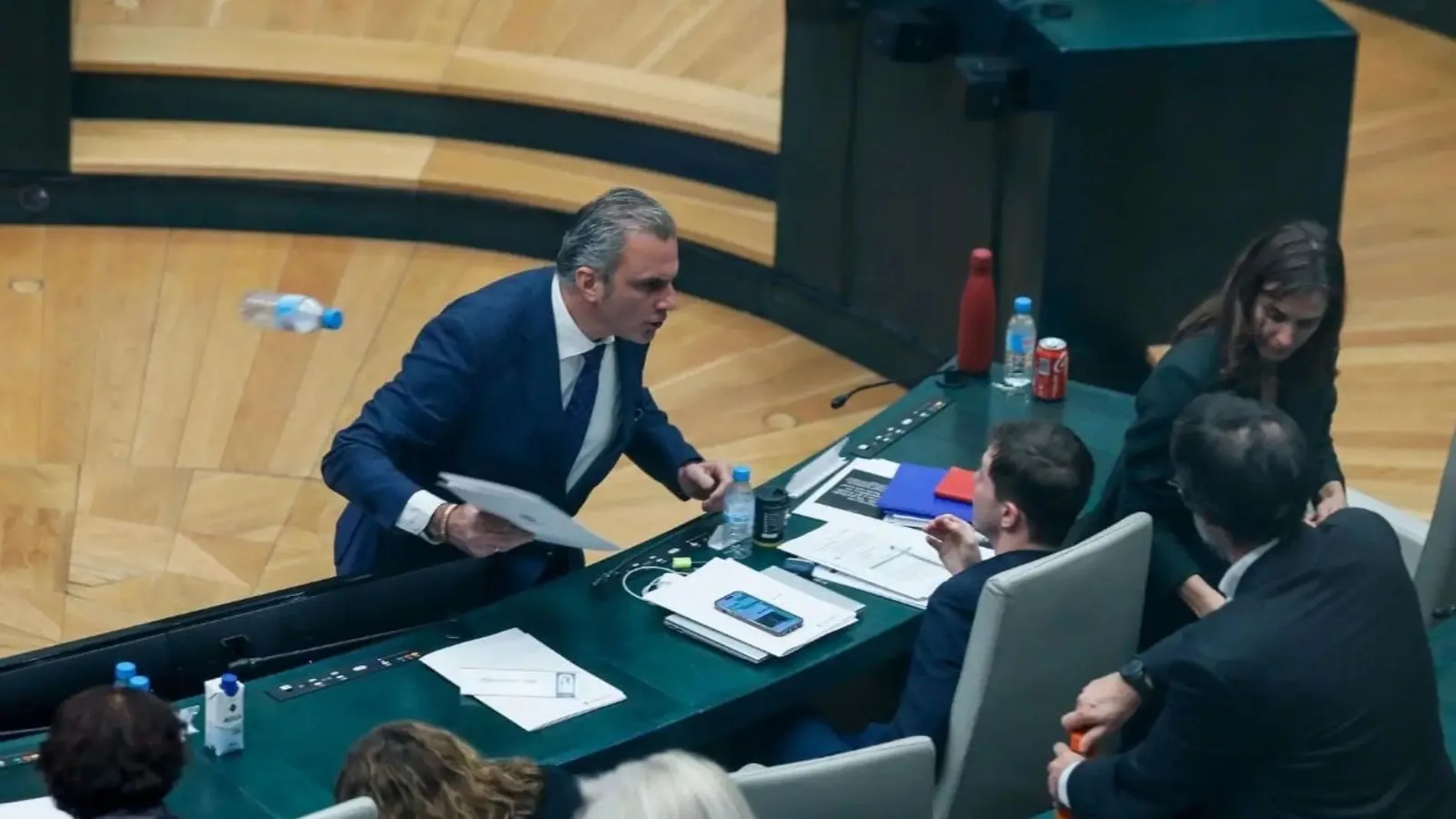 Momento en el que el portavoz de Vox en el Ayuntamiento de Madrid, Javier Ortega Smith, se encara y tira unos papeles y una botella de agua vacía al edil Eduardo Fernández Rubiño, concejal de Más Madrid, en su escaño. | Europa Press