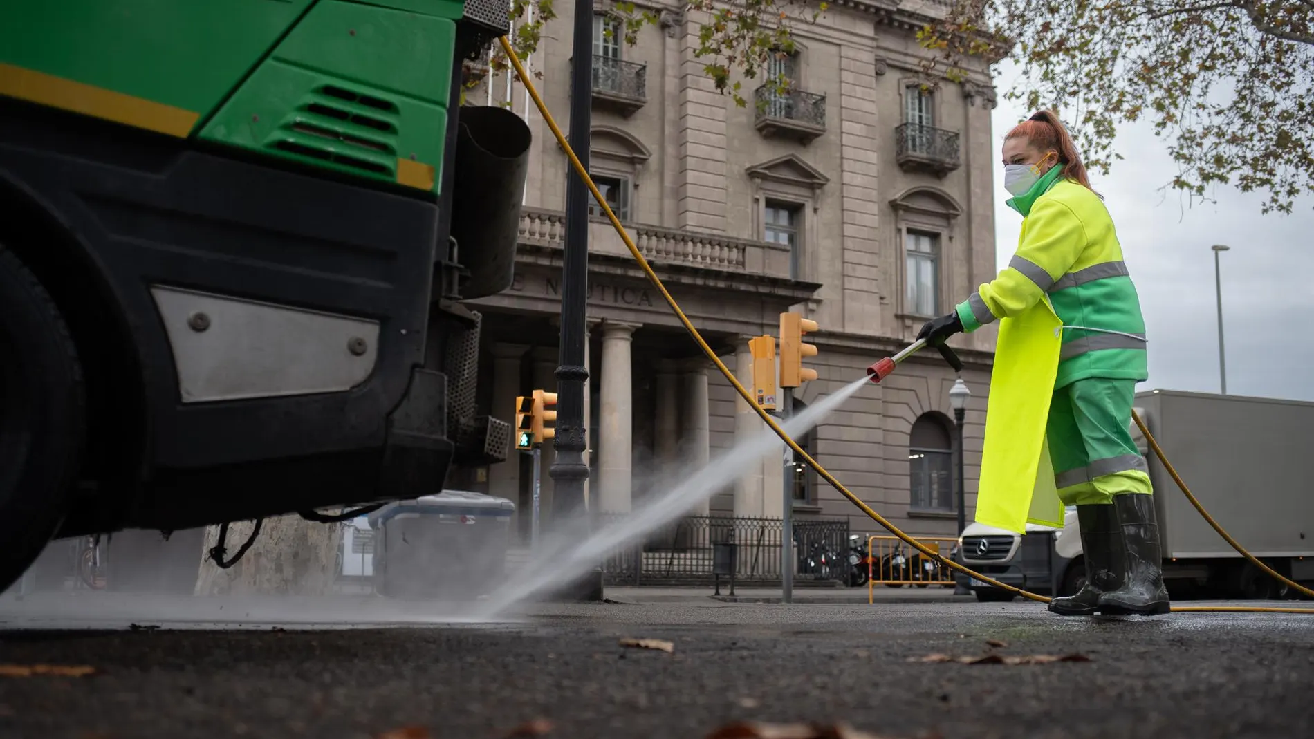 Una trabajadora riega una calle con una manguera en enero