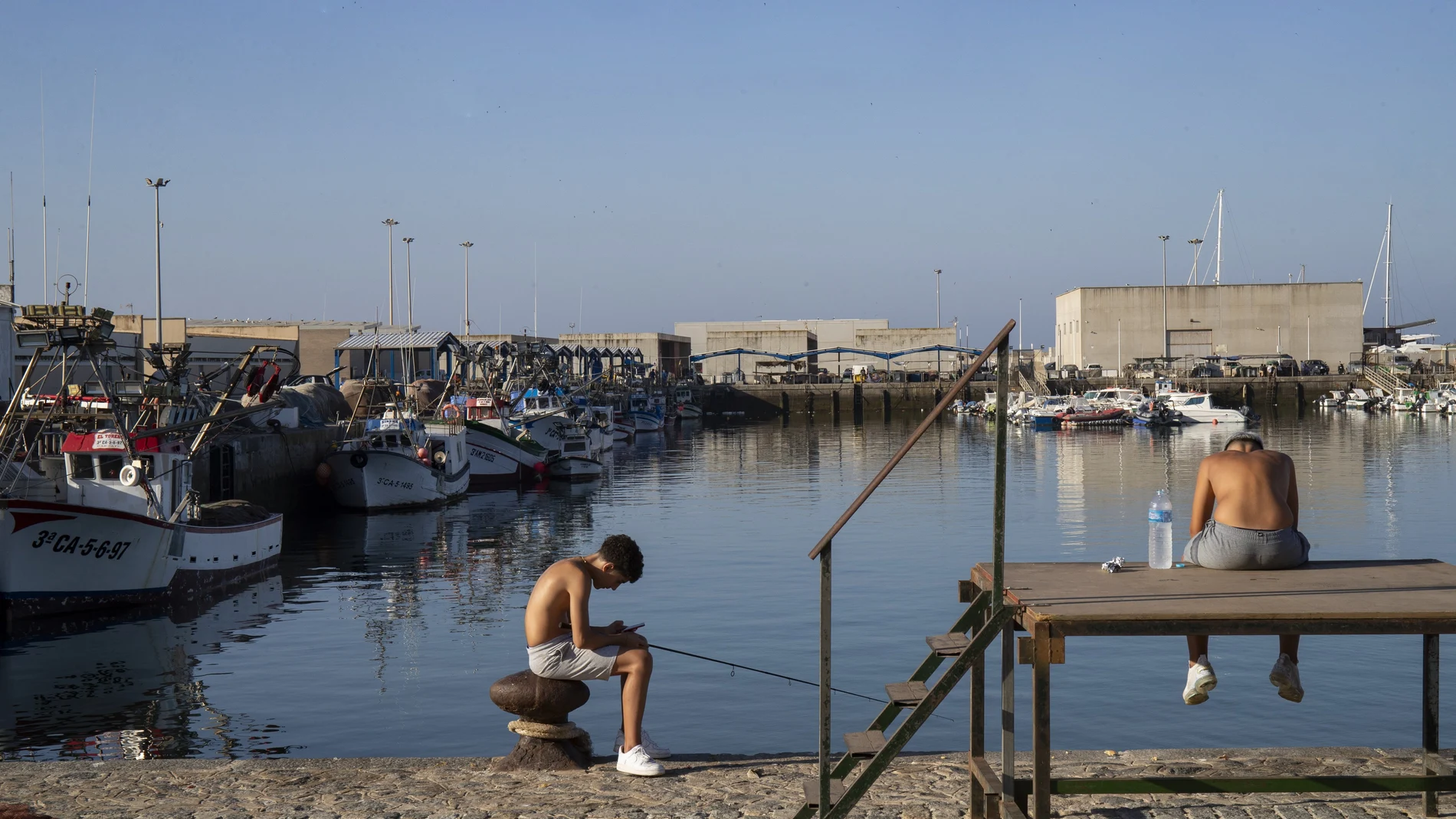 GRAFAND3854. BARBATE (CÁDIZ), 17/07/2023.- Unos jóvenes pescan en el muelle pesquero de Barbate(Cádiz). La falta de pescado en el caladero y el elevado precio del combustible, entre otras circunstancias, han hecho que el acuerdo pesquero entre la UE y Marruecos que expira este lunes no haya sido rentable para los pesqueros de las localidades gaditanas de Barbate y Conil de la Frontera que lo usan para faenar en las aguas vecinas y que hoy se concentran para expresar la crítica situación en la que se encuentra el sector. EFE/Román Ríos
