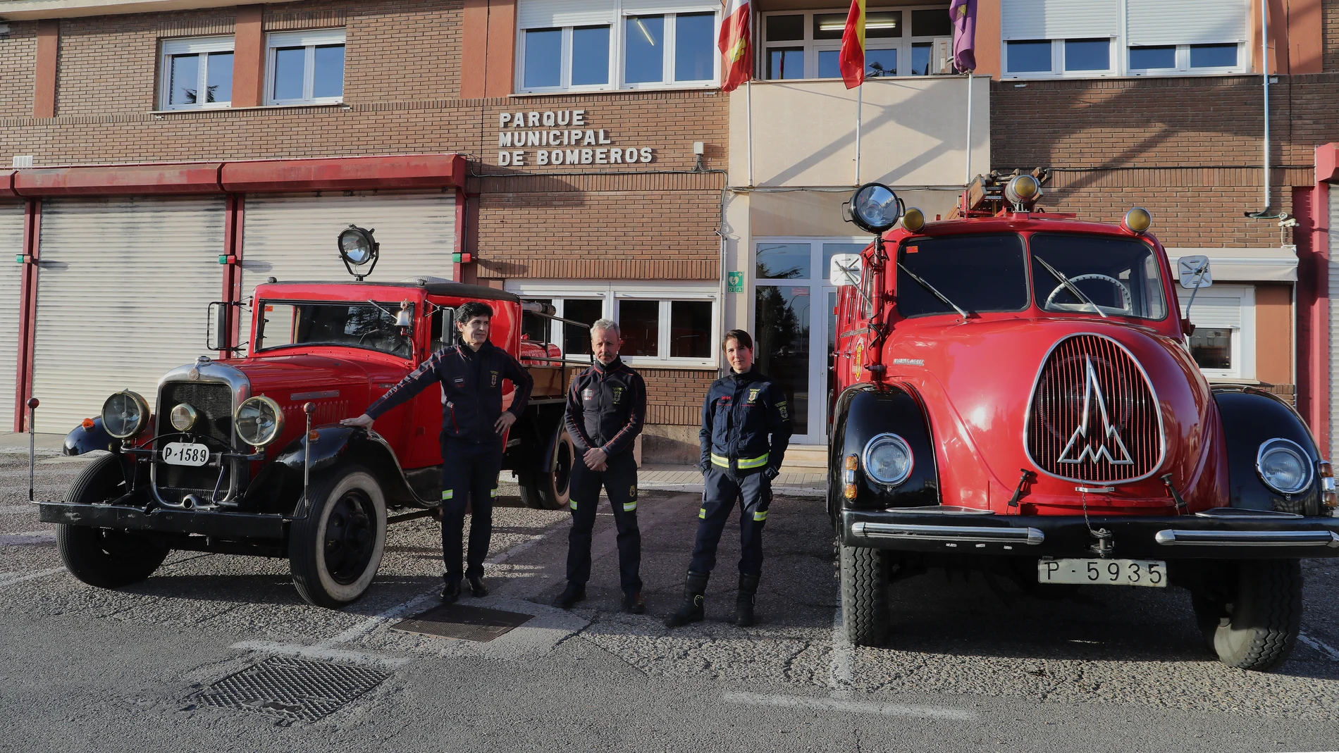 El jefe del parque de bomberos, Javier Villena(C), el sargento Abel Allende(I), y la bombera Isabel Villán junto a los dos camiones antiguos conocidos el Abuelo y la Abuela