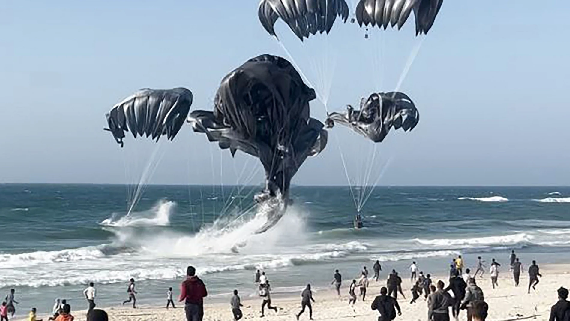 This image grab from an AFPTV video shows Palestinians running toward parachutes attached to food parcels, air-dropped from US aircrafts on a beach in the Gaza Strip on March 2, 2024.
