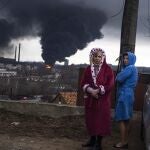 Women stand in their robes as smoke rises in the background after shelling in Odesa, Ukraine, Sunday, April 3, 2022. (AP Photo/Petros Giannakouris)