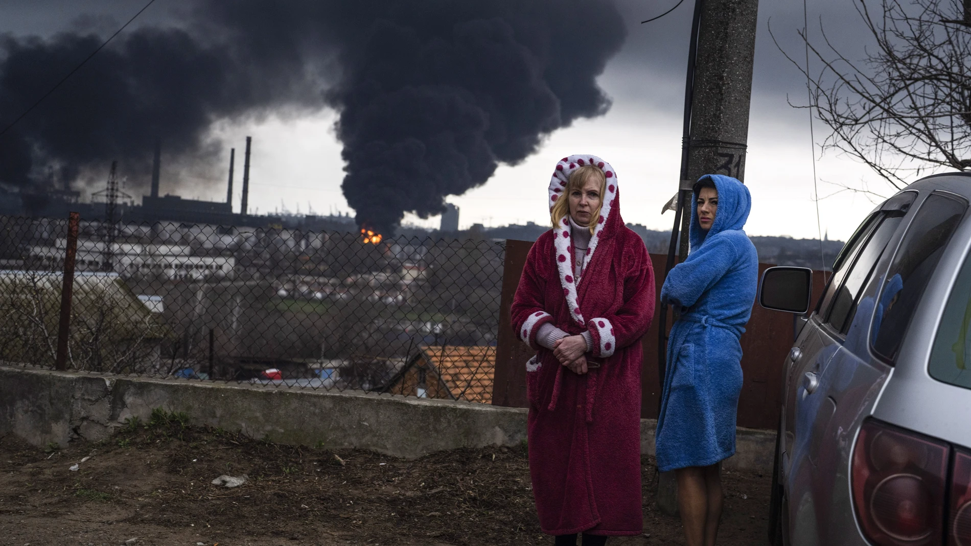 Women stand in their robes as smoke rises in the background after shelling in Odesa, Ukraine, Sunday, April 3, 2022. (AP Photo/Petros Giannakouris)
