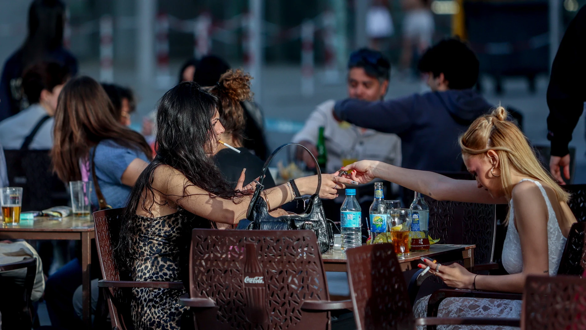 Una mujer le pasa el mechero a otra en una terraza