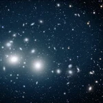 Esta imagen, capturada por el satélite Euclid, muestra el cúmulo de galaxias de Perseo bañado en una suave luz azul emanada de las estrellas huérfanas. Estas estrellas huérfanas están dispersas por todo el cúmulo, extendiéndose hasta 2 millones de años luz desde su centro. Las galaxias del cúmulo destacan como formas elípticas luminosas contra la oscura extensión del espacio. 