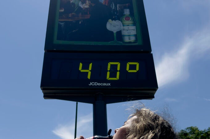 Una mujer bebe un refresco junto a un termómetro que marca 40 grados