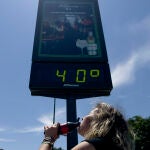Una mujer bebe un refresco junto a un termómetro que marca 40 grados