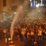 Imagen de los bomberos mojando al público que observa como arde un monumento fallero en la noche del 24 de junio, en la cremà