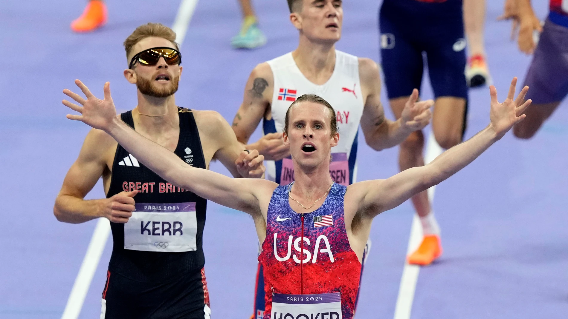 Cole Hocker, of the United States, crosses the finish line ahead of Josh Kerr, of Britain, and fourth placed Jakob Ingebrigtsen, of Norway, in the background, to win the men's 1500 meters final at the 2024 Summer Olympics, Tuesday, Aug. 6, 2024, in Saint-Denis, France. (AP Photo/Martin Meissner)
