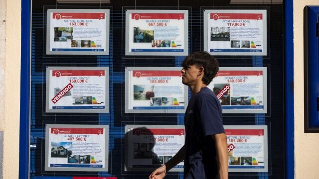 Joven pasando al lado de una inmobiliaria. 