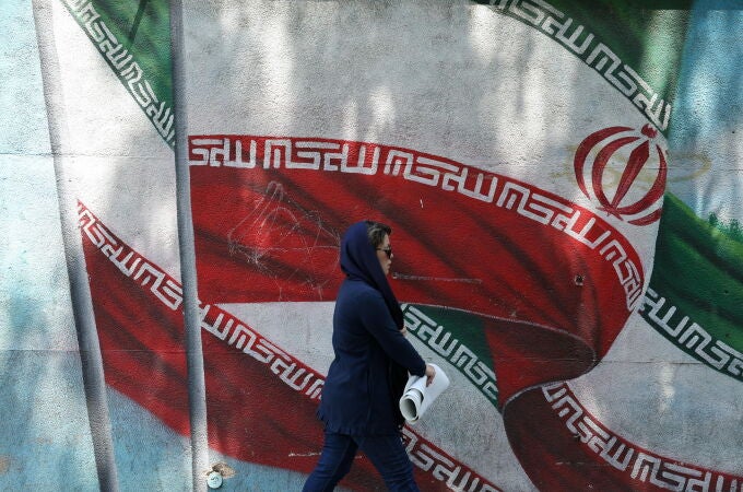 Una mujer pasa junto a un mural de la bandera de Irán en Teherán
