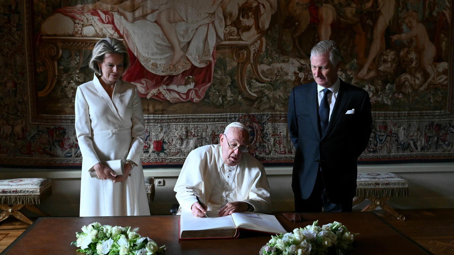 Pope Francis, center, signs the book of honor during his visit to King Philippe of Belgium, right, and Queen Mathilde at the Castle of Laeken, Belgium, Friday, Sept. 26, 2024, on the second day of a four-day apostolic journey to Luxembourg and Belgium. (Alberto Pizzoli/pool photo via AP)
