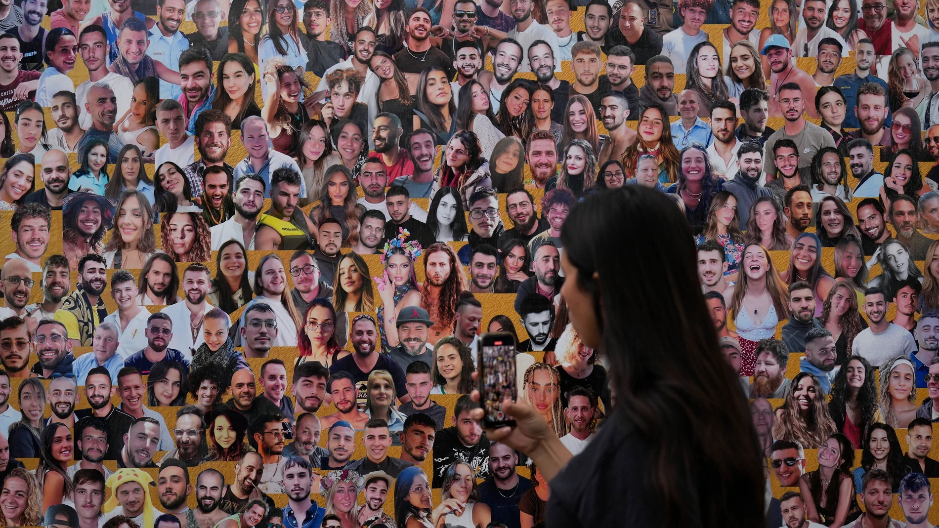 An attendant walks through a mural with portraits of the victims at the site of the Nova music festival, where hundreds of revelers were killed and abducted by Hamas and taken into Gaza, on the one-year anniversary of the attack, near Kibbutz Reim, southern Israel, Monday, Oct. 7, 2024. (AP Photo/Ariel Shalit)