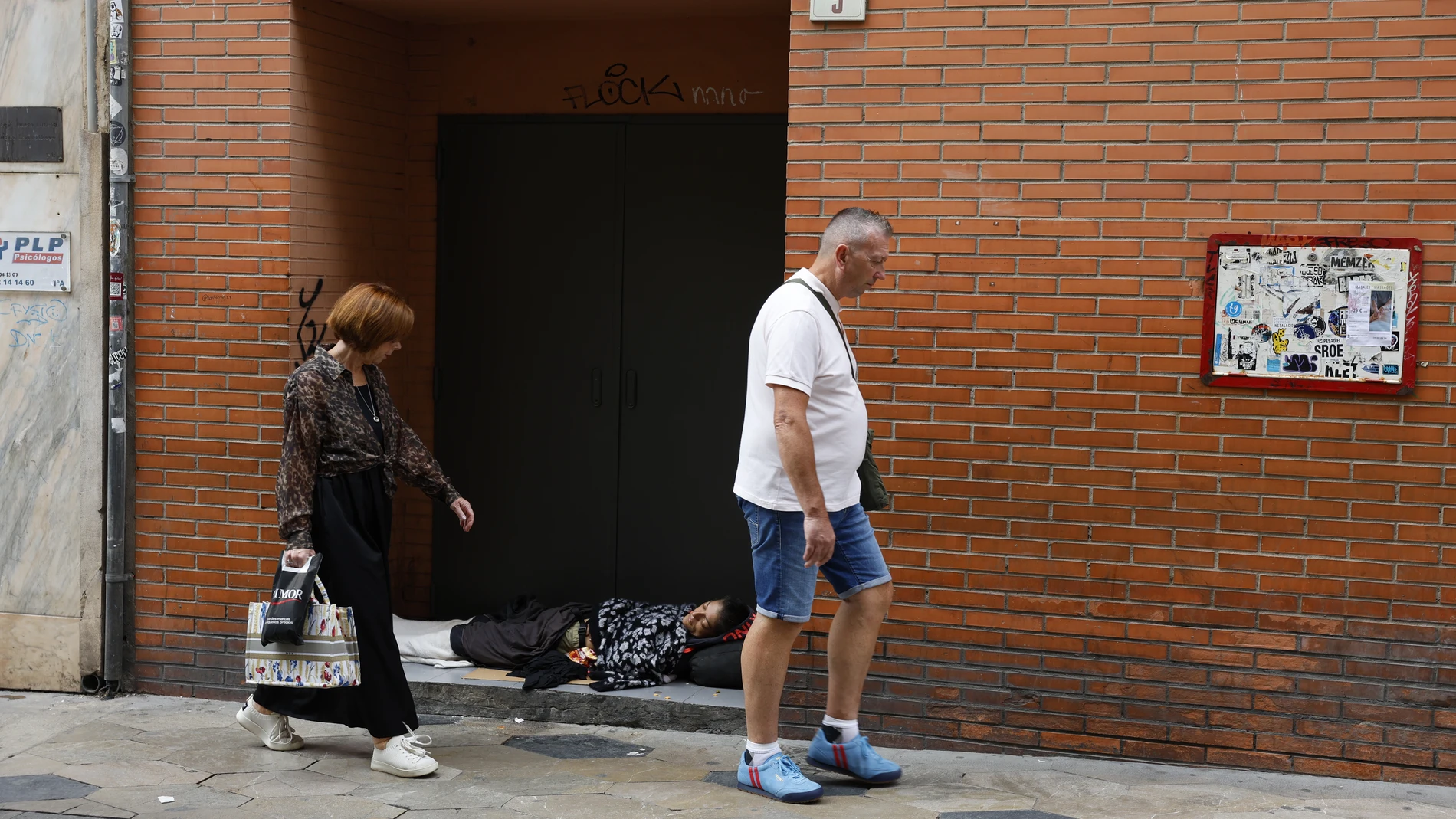MA01. MÁLAGA, 15/10/2024.-Dos personas que caminan por una calle de Málaga observan a una sintecho acostada en un portal.Un total de 3,2 millones de personas de la población andaluza se encuentra en riesgo de pobreza y/o exclusión social, lo que supone un 37,5 % del total de habitantes de la región, que ocupa el puesto más elevado de todas las comunidades en cuatro de los cinco principales indicadores de pobreza.EFE/Jorge Zapata