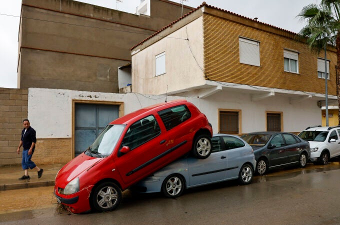 Una persona pasa junto a unos coches amontonados debido a las lluvias torrenciales que afectan a la Comunitat Valenciana, y especialmente a la provincia de Valencia