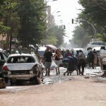 VALENCIA, 30/10/2024.- Unas personas caminan por una calle cubierta de lodo y llena de coches amontonados tras las intensas lluvias por la fuerte DANA hoy en Valencia