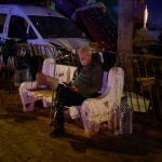 Un hombre consulta su teléfono en un banco de una calle en Paiporta, en Valencia
