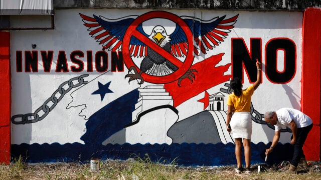 Una pareja de panameños pinta un mural contra la invasión a Panamá por parte de Los Estados Unidos este miércoles, en la provincia de Colón (Panamá). 25 años después de que el canal fuera transferido por Estados Unidos a Panamá, la vía "no ha parado de crecer", como defiende el Gobierno panameño, con más toneladas en tránsito y aportes económicos al Estado, que se enfrenta ahora a las amenazas del presidente Donald Trump, que no descarta el uso de la fu...