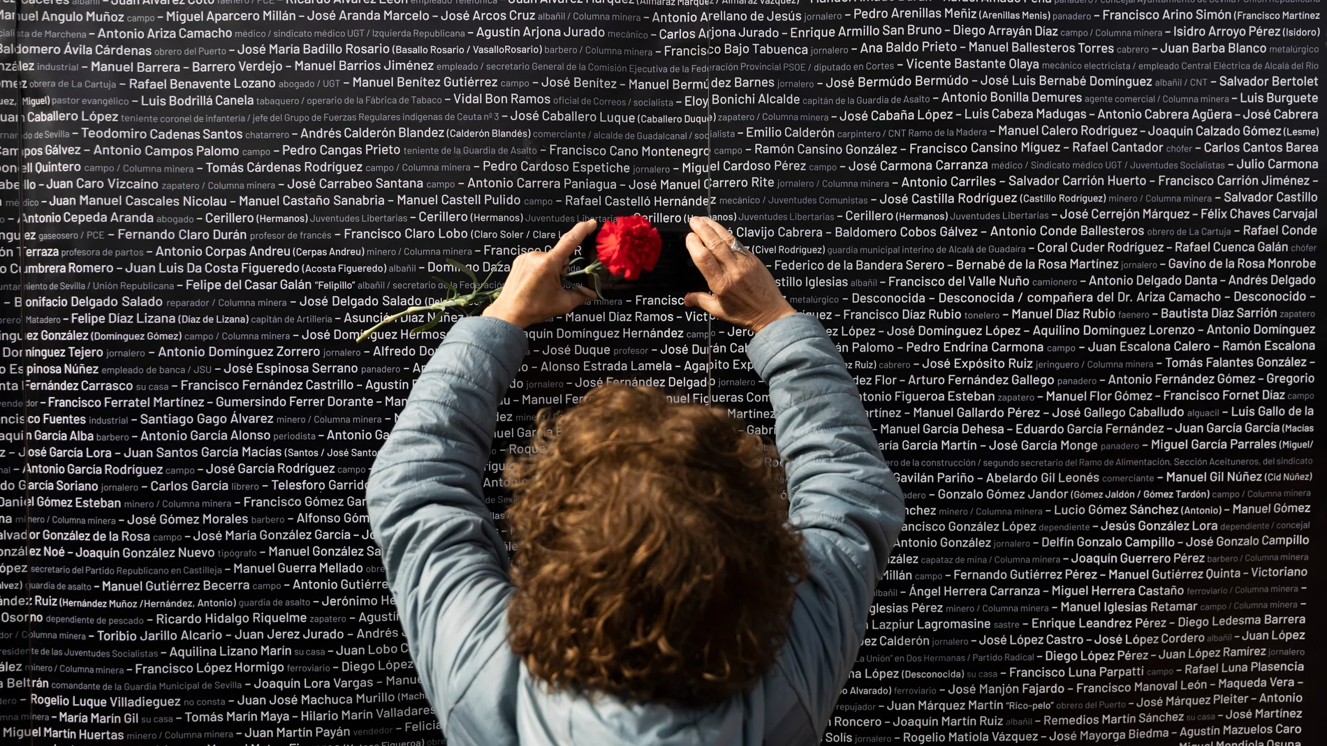 Una mujer hace una foto del nombre de su familiar, colocado en un panel junto a los nombres de las demás víctimas de la fosa de Pico Reja