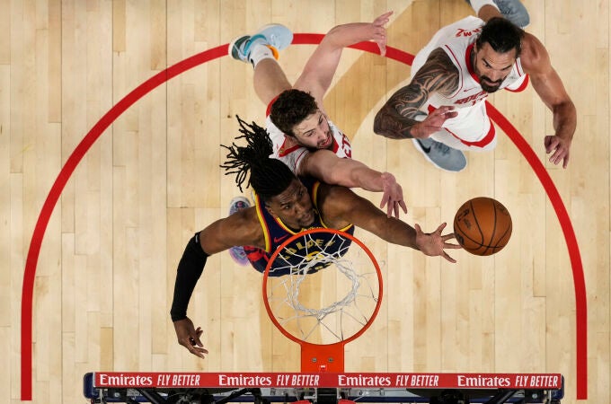 Kevon Looney intenta hacerse con un rebote en presencia de dos jugadores de los Rockets
