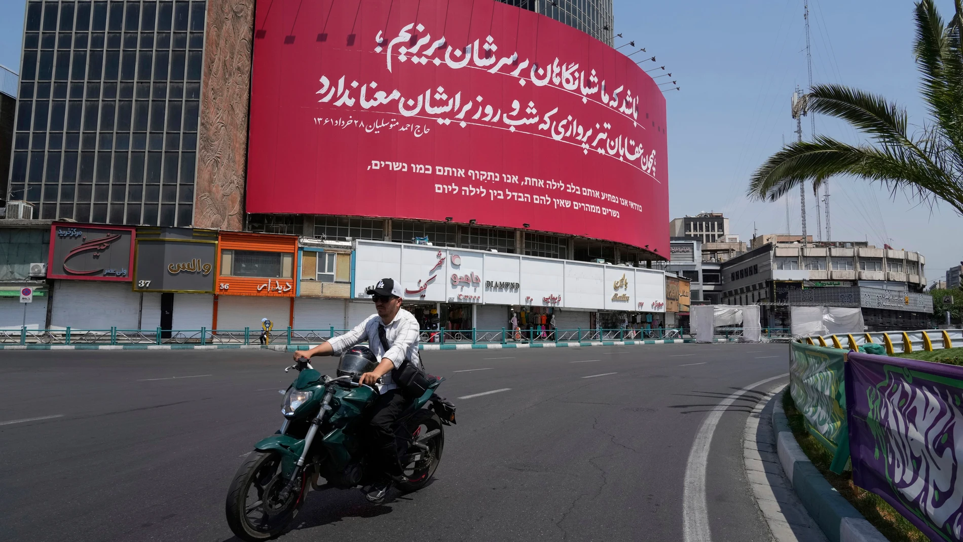 A man rides his motorbike past an anti-Israeli banner that reads in Farsi and Hebrew: 'May we swoop down on them under the cover of night like swift-flying eagles, for whom night and day hold no meaning,' at Vali-e-Asr Square in Tehran, Iran, Saturday, June 14, 2025. (AP Photo/Vahid Salemi)