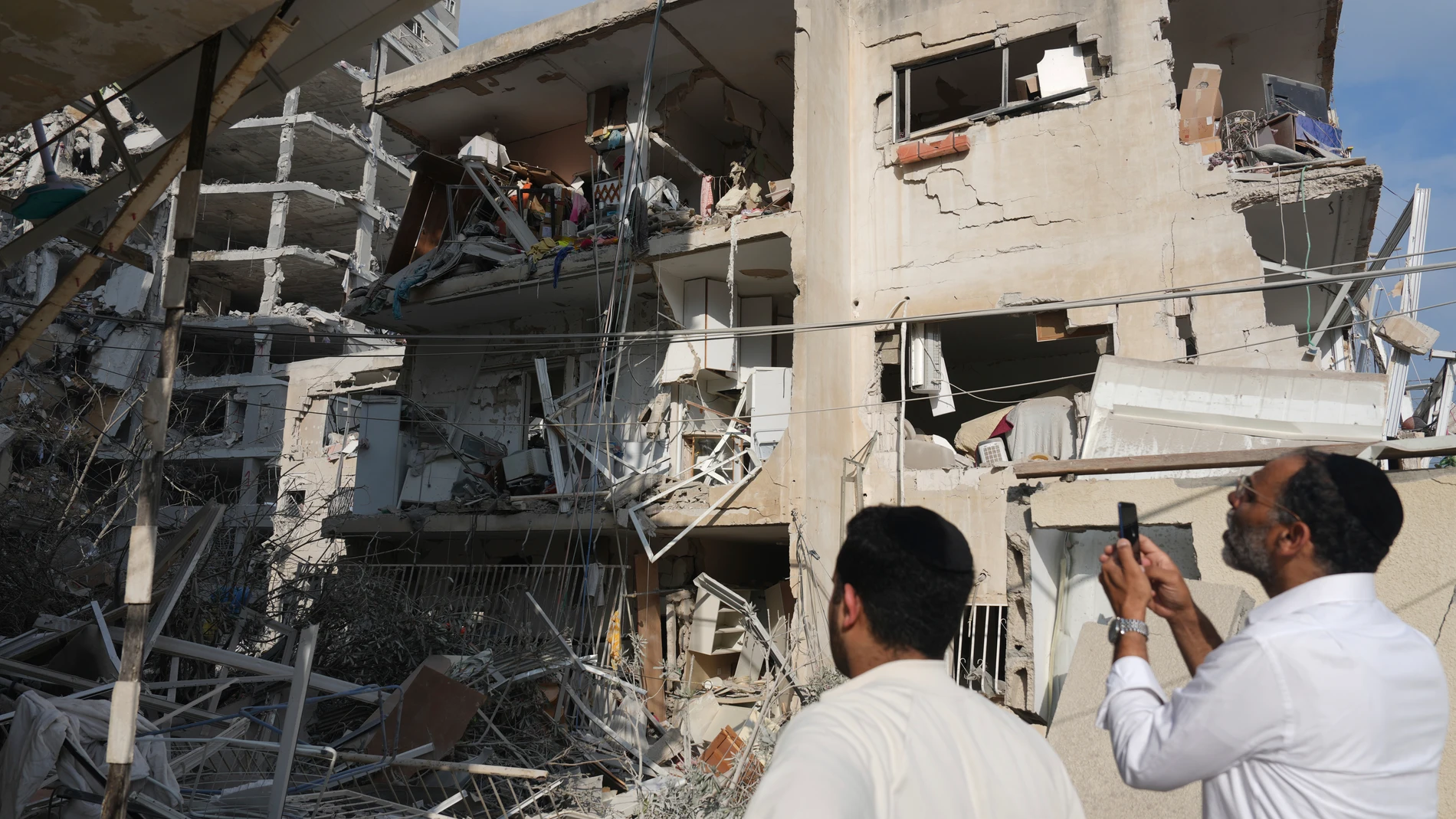 People inspect a destroyed building that was hit by a missile fired from Iran, near Tel Aviv, Israel, Sunday, June 15, 2025. (AP Photo/Ariel Schalit)