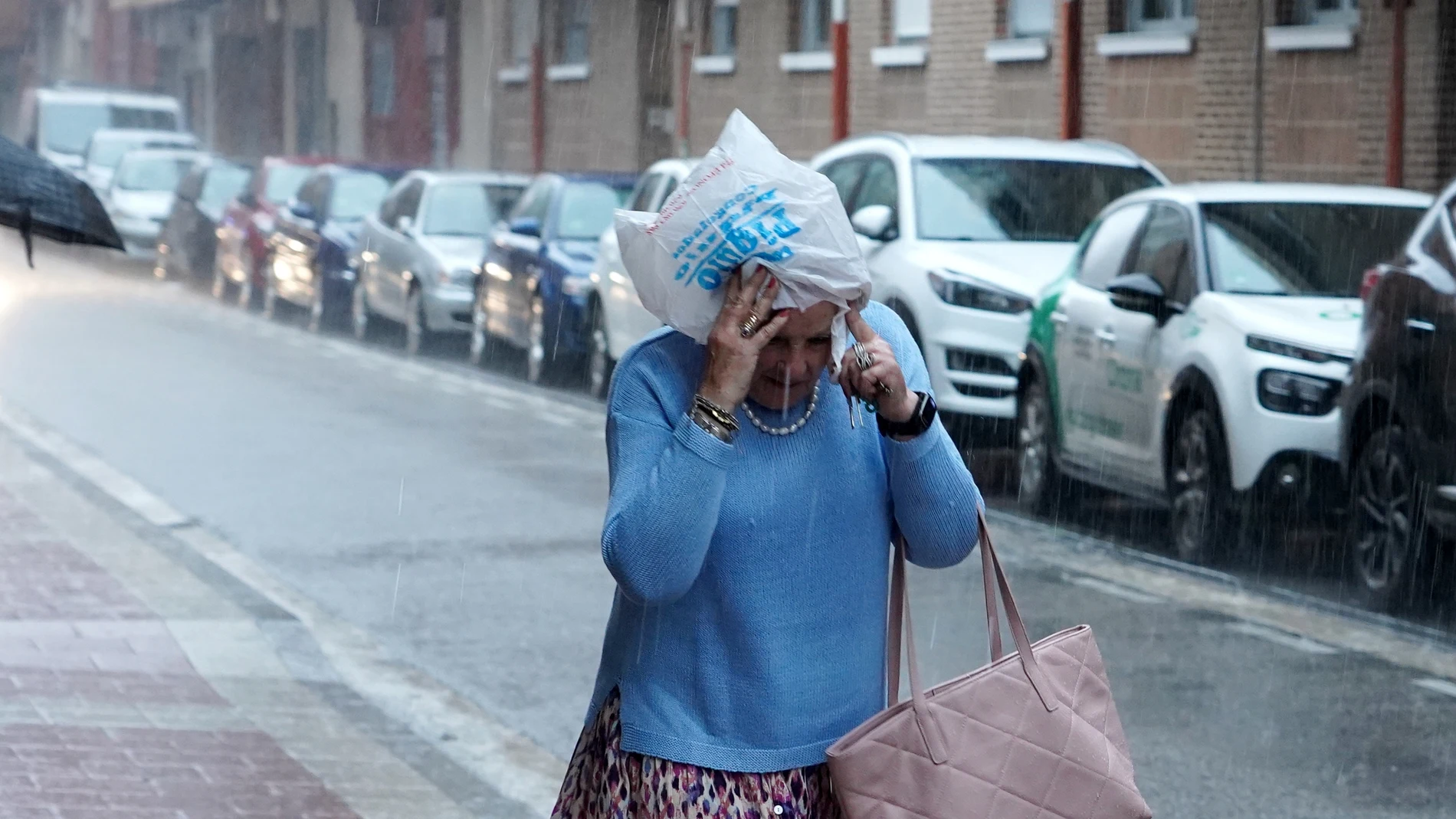 Una mujer se tapa la cabeza con una bolsa durante una fuerte tormenta en Valladolid