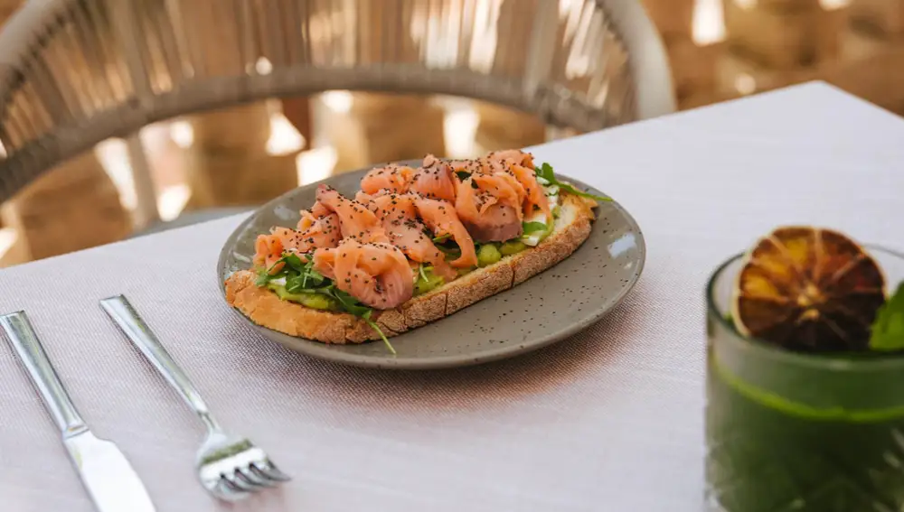 tostada de pan de espelta integral con guacamole, queso fresco, salmón ahumado, rúcula y semillas.