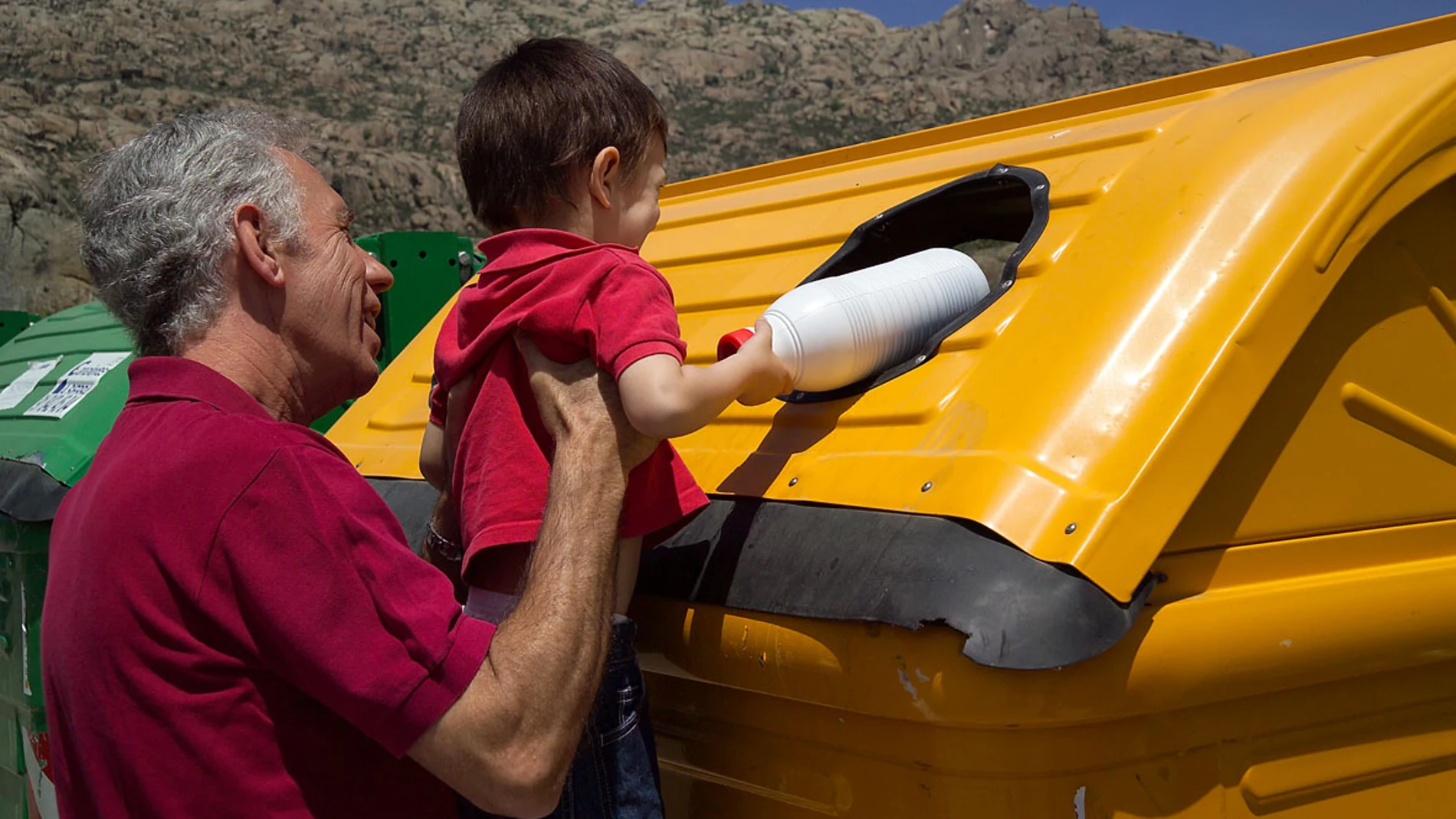 Padre e hijo reciclajdo un envase de plástico en contenedor en una playa entorno natural en verano