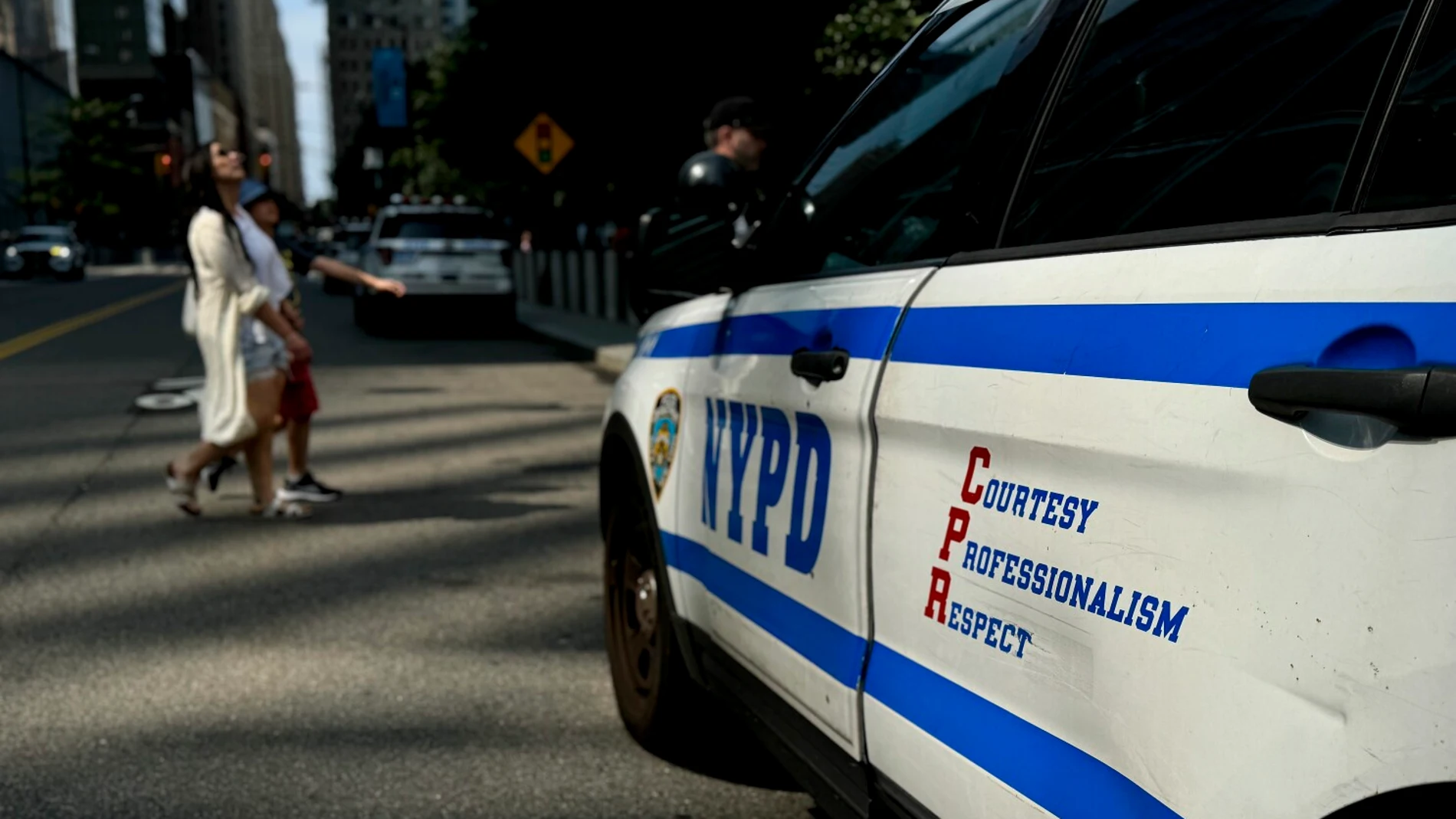 Aparece el perfil de un coche de policía blanco y azul con las siglas NYPD (New York Police Departament)