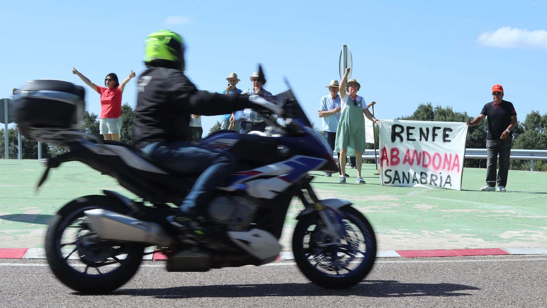 EL PUENTE DE SABABRIA (ZAMORA), 12/07/2025.- Uno de los moteros participantes en la primera ruta de la XXXI Concentración Internacional de Motos del Lago de Sanabria pasa ante varias personas que reivindican la parada sanabresa del AVE Madrid-Galicia, este sábado. EFE/Mariam A. Montesinos