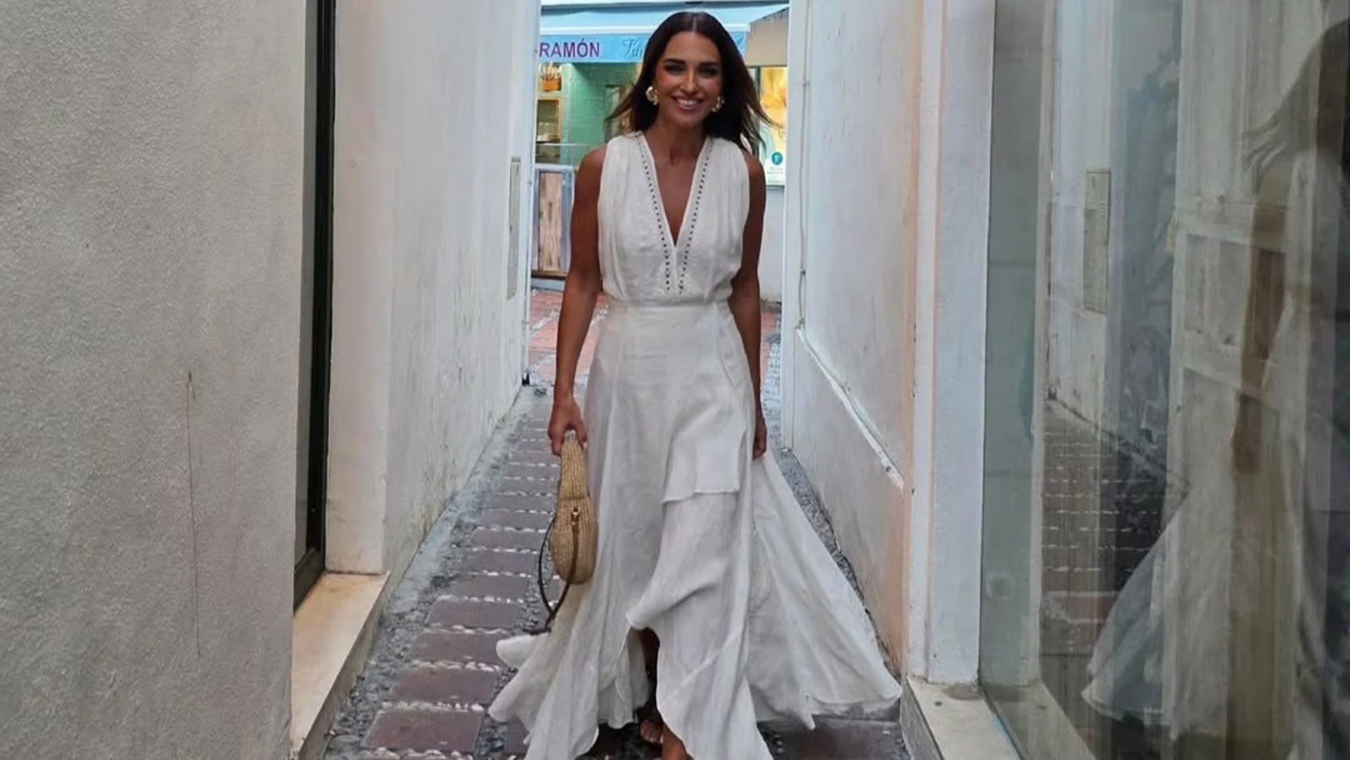 Paula Echevarría con vestido blanco largo y escote en pico caminando por una calle estrecha en un look veraniego y elegante