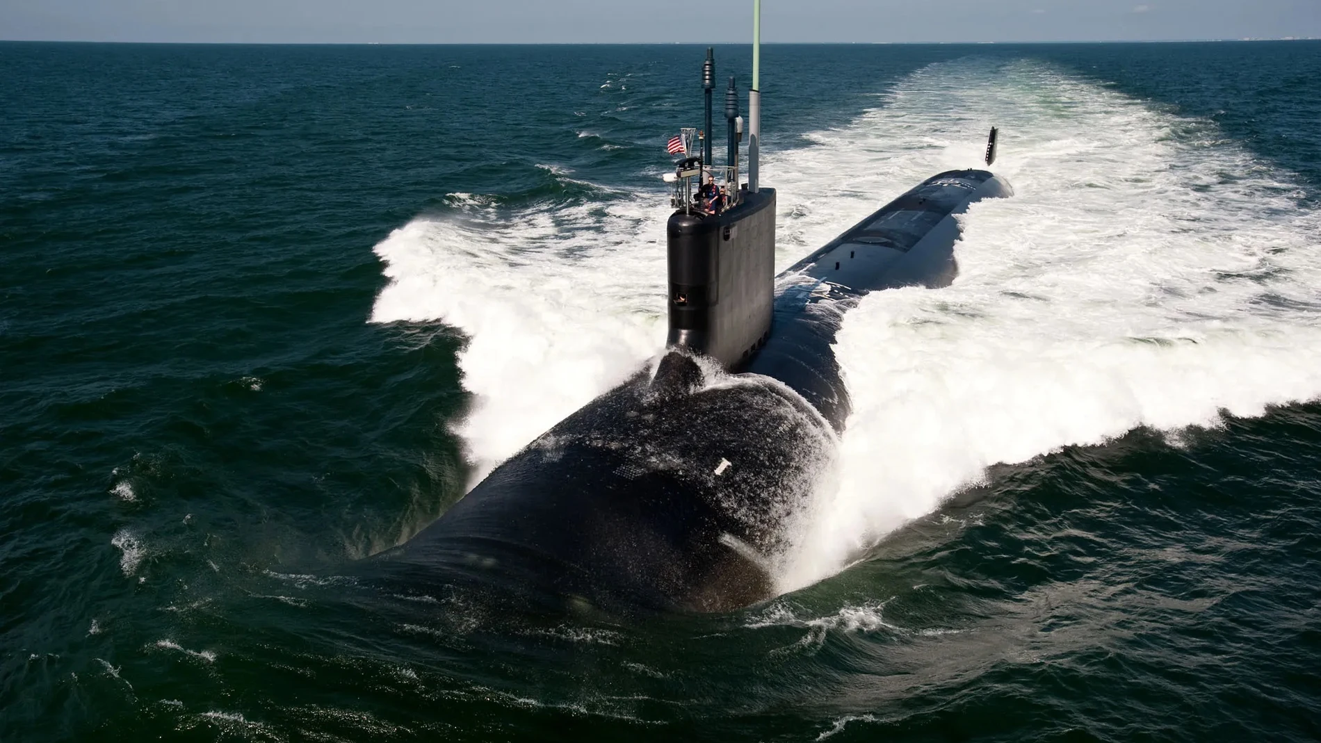 Aparece un submarino en alta mar con la escotilla abierta y un soldado mirando el horizonte bajo la bandera de Estados Unidos