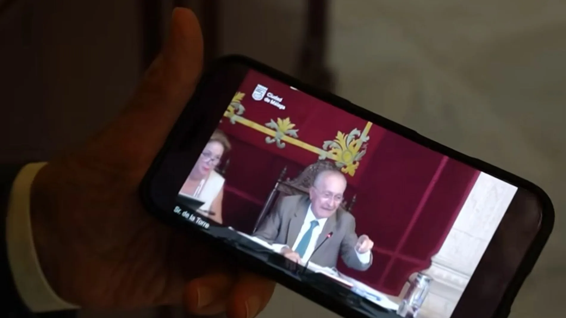 El alcalde de Málaga sujeta un teléfono móvil en el que reproduce el vídeo viral del pleno de julio