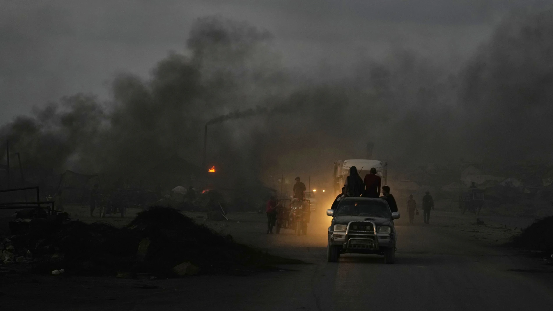 Palestinos conducen sus vehículos entre el humo negro proveniente de quemadores improvisados utilizados para extraer combustible del plástico derretido a lo largo de la Carretera del Mar, al anochecer en el sur de la ciudad de Gaza