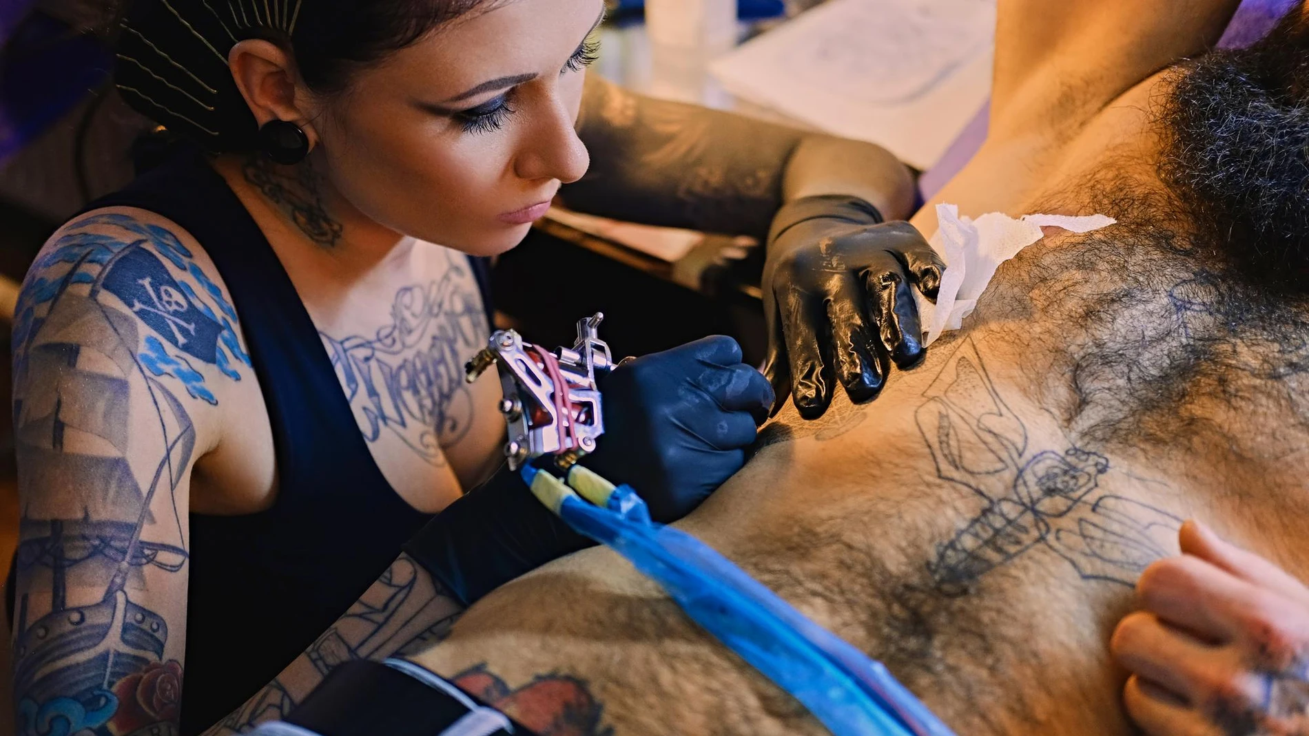 Una tatuadora trabaja la piel de su cliente con tintas de tatuaje con riesgos y precauciones