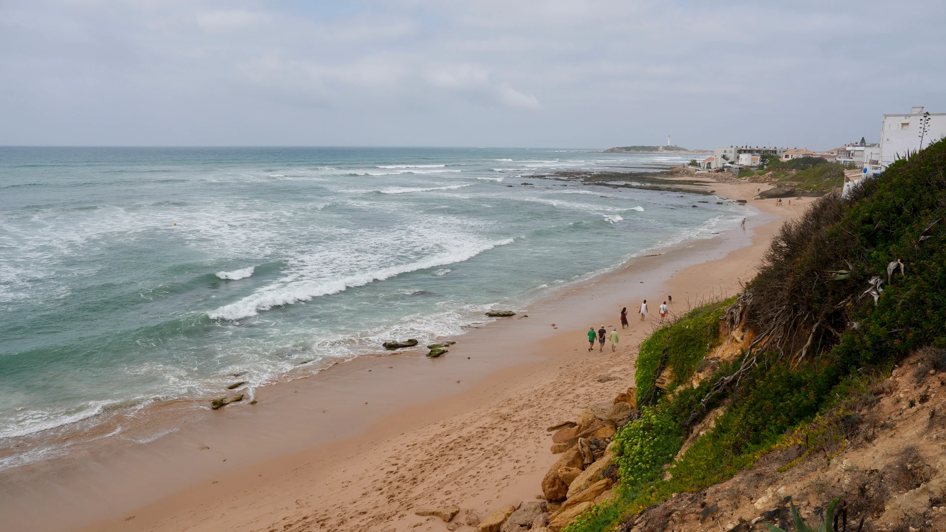 GRAF3314. BARBATE (CÁDIZ), 27/08/2025.- Unas personas pasean por la playa de Los Caños de Meca que pertenece al municipio de Barbate en Cádiz tras la fuerte marejada que sufrió ayer por la tarde que provocó grandes olas que arrastraron chiringuitos e infraestructuras, y que permanece cerrada con bandera roja. EFE/Román Ríos.